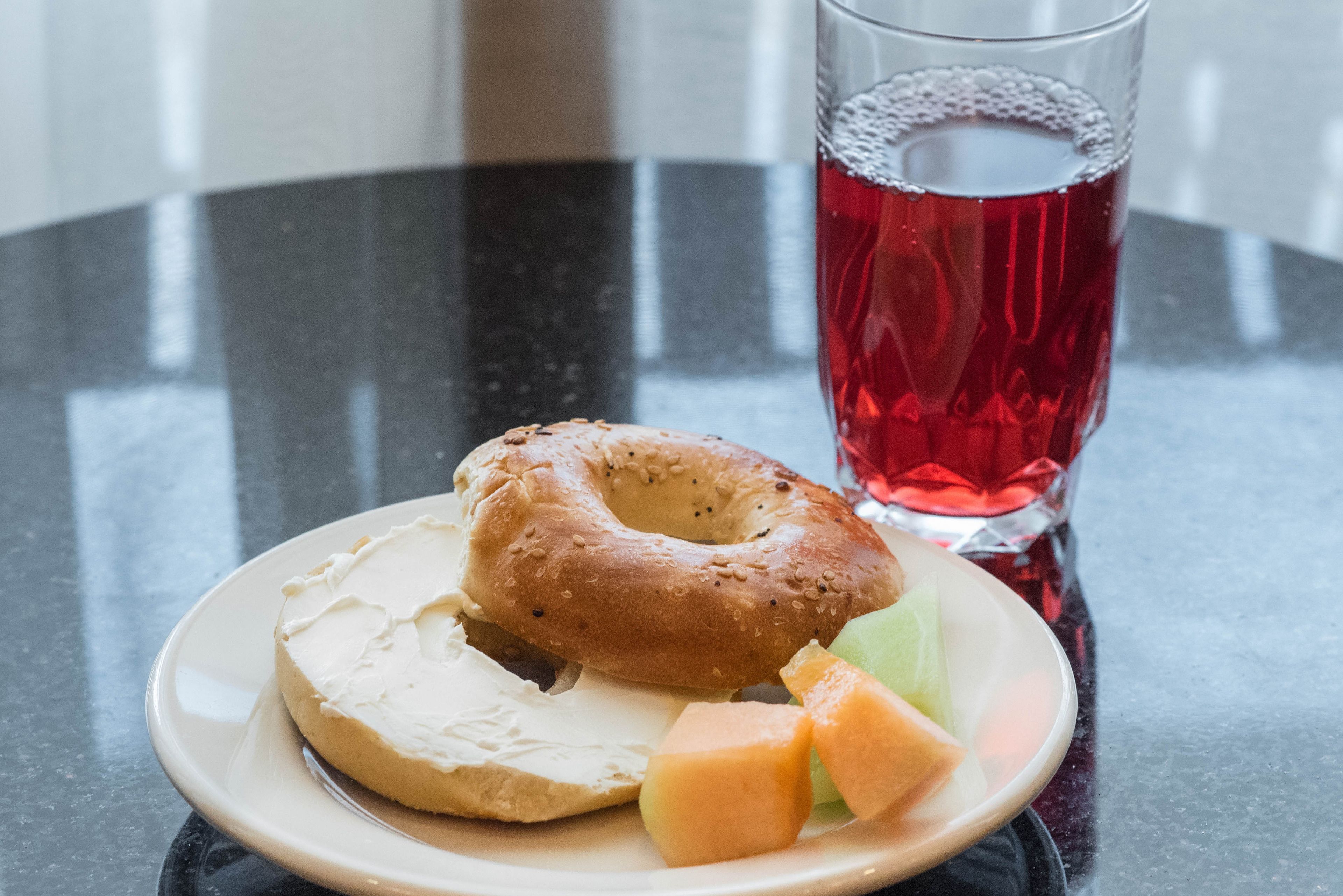 A plate with a bagel, cream cheese, and melon slices on a table.