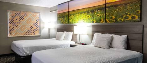 A hotel room with two beds, a large painting of a sunflower field, and a geometric patterned wall.