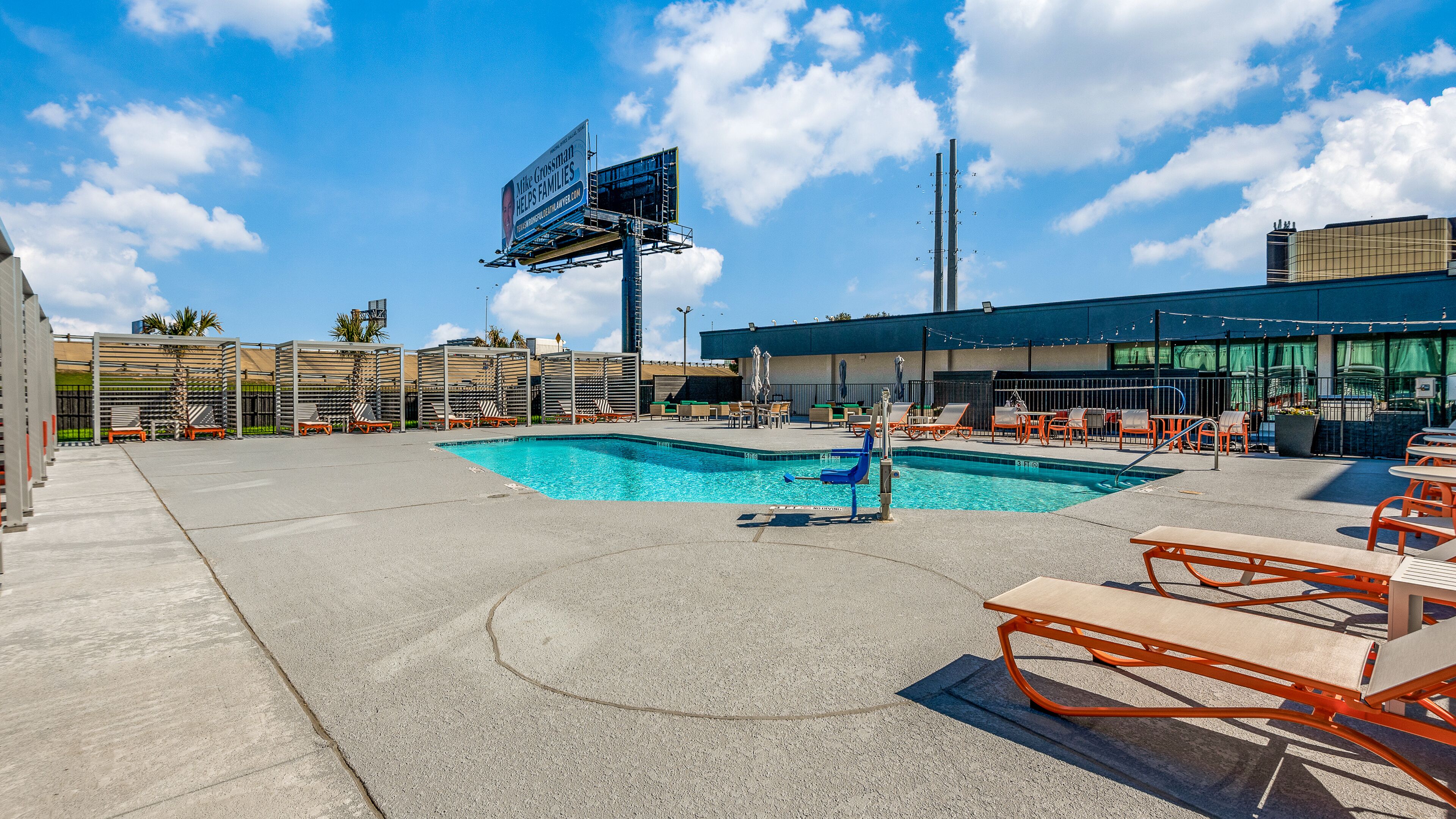 Un espace piscine aménagé sur le toit, avec des chaises longues, une piscine et un panneau publicitaire.
