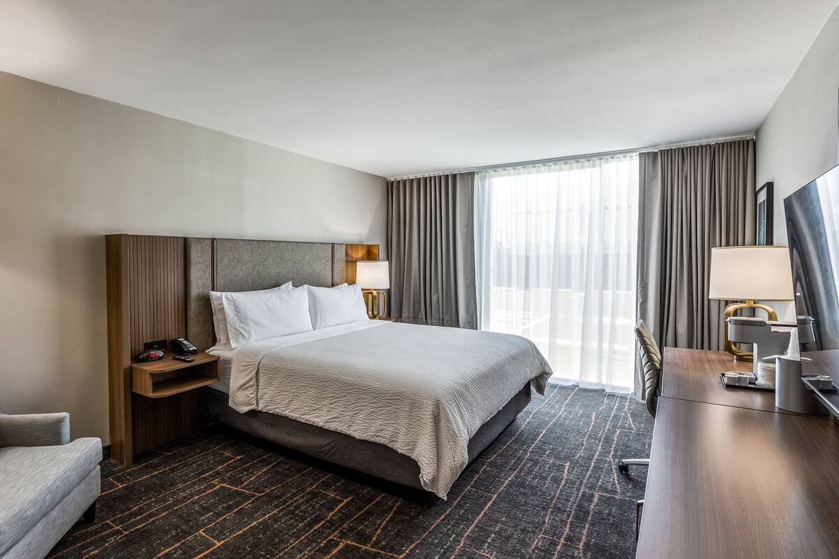 Une chambre d’hôtel avec un grand lit, un bureau avec une lampe, une chaise et une table de chevet avec un téléphone et une télécommande.