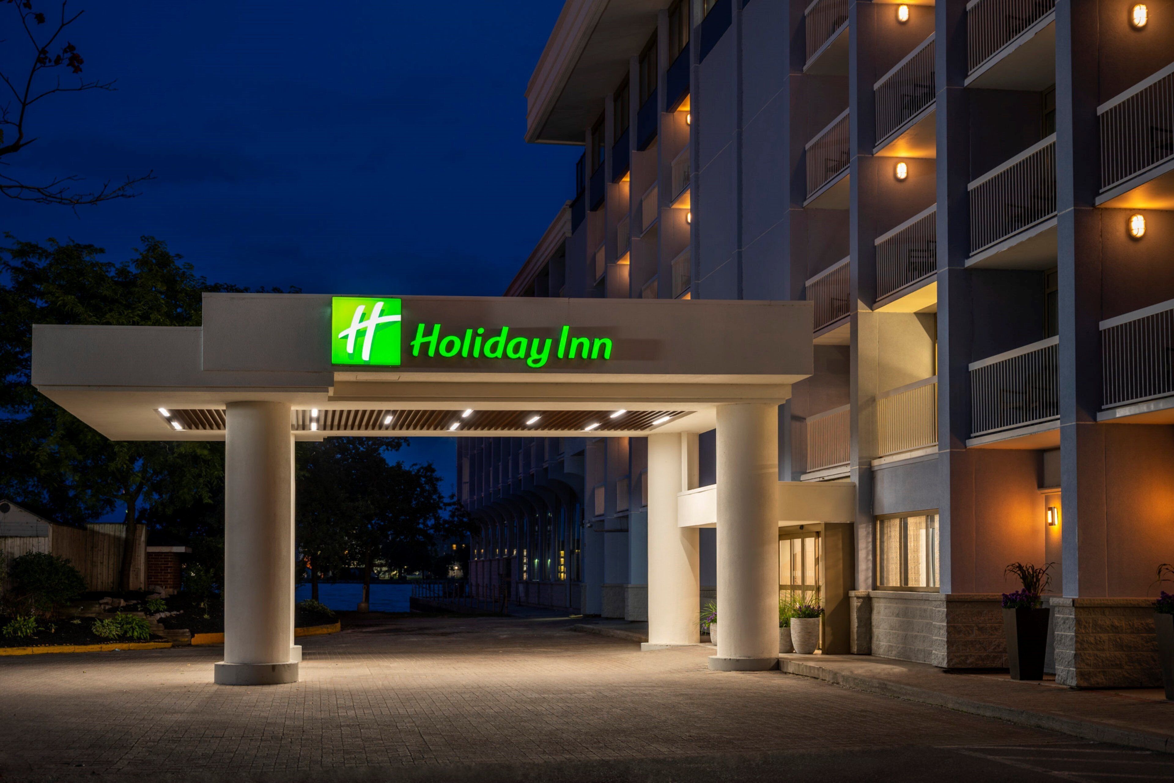 L’entrée d’un hôtel Holiday Inn, dotée d’un design moderne, se caractérise par une enseigne verte bien visible, une allée couverte et un bâtiment agrémenté de nombreux balcons.