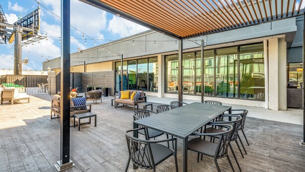 An outdoor patio with a wooden pergola, a dining table with chairs, and a seating area with sofas and cushions.