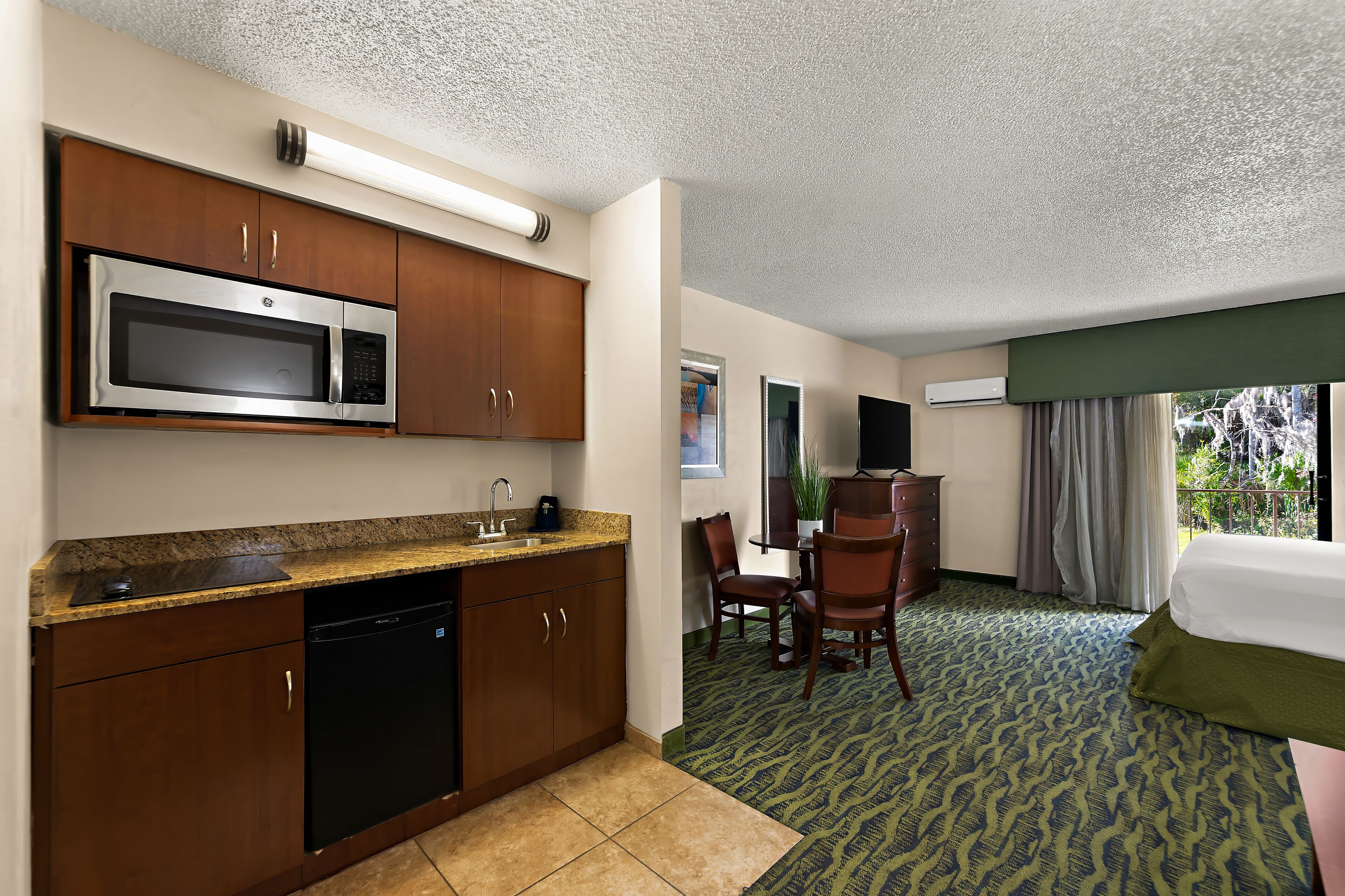 A hotel room with a kitchenette, a dining area, and a bed.