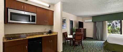 A hotel room with a kitchenette, a dining area, and a bed.