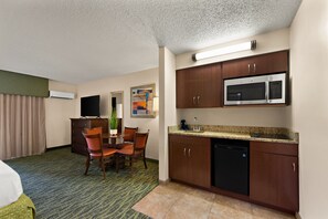 A hotel room with a dining area, kitchenette, and a bed.