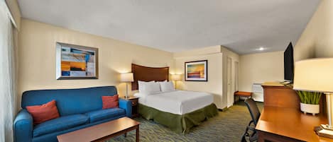 A hotel room with a bed, a blue sofa, a wooden desk, a chair, and a small table.