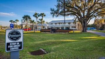 A grassy area with a sign for Grassroots Coffee, a building with a boat in front, and a clear blue sky.