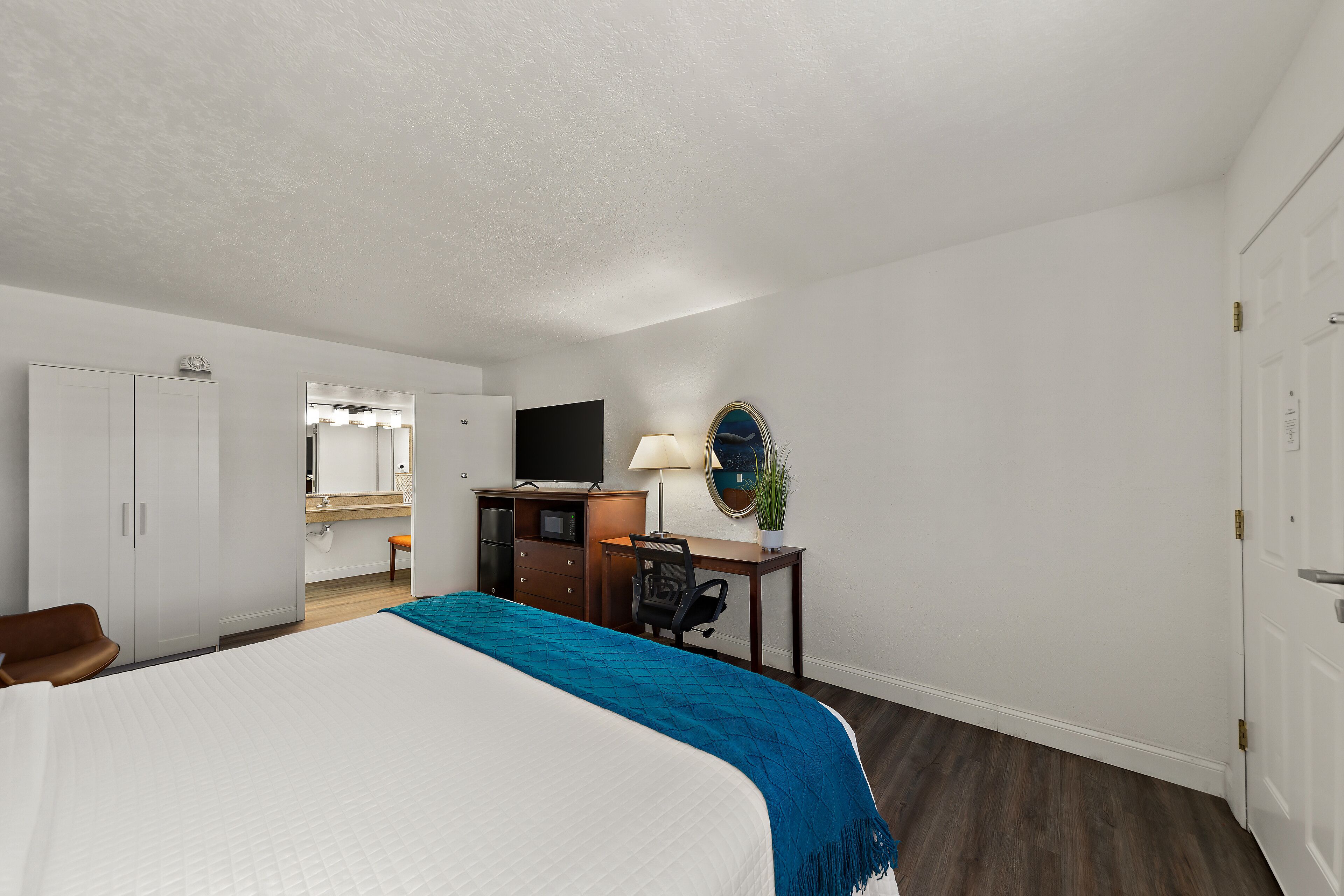 A hotel room with a bed, a desk, a chair, a television, a mirror, and a door.