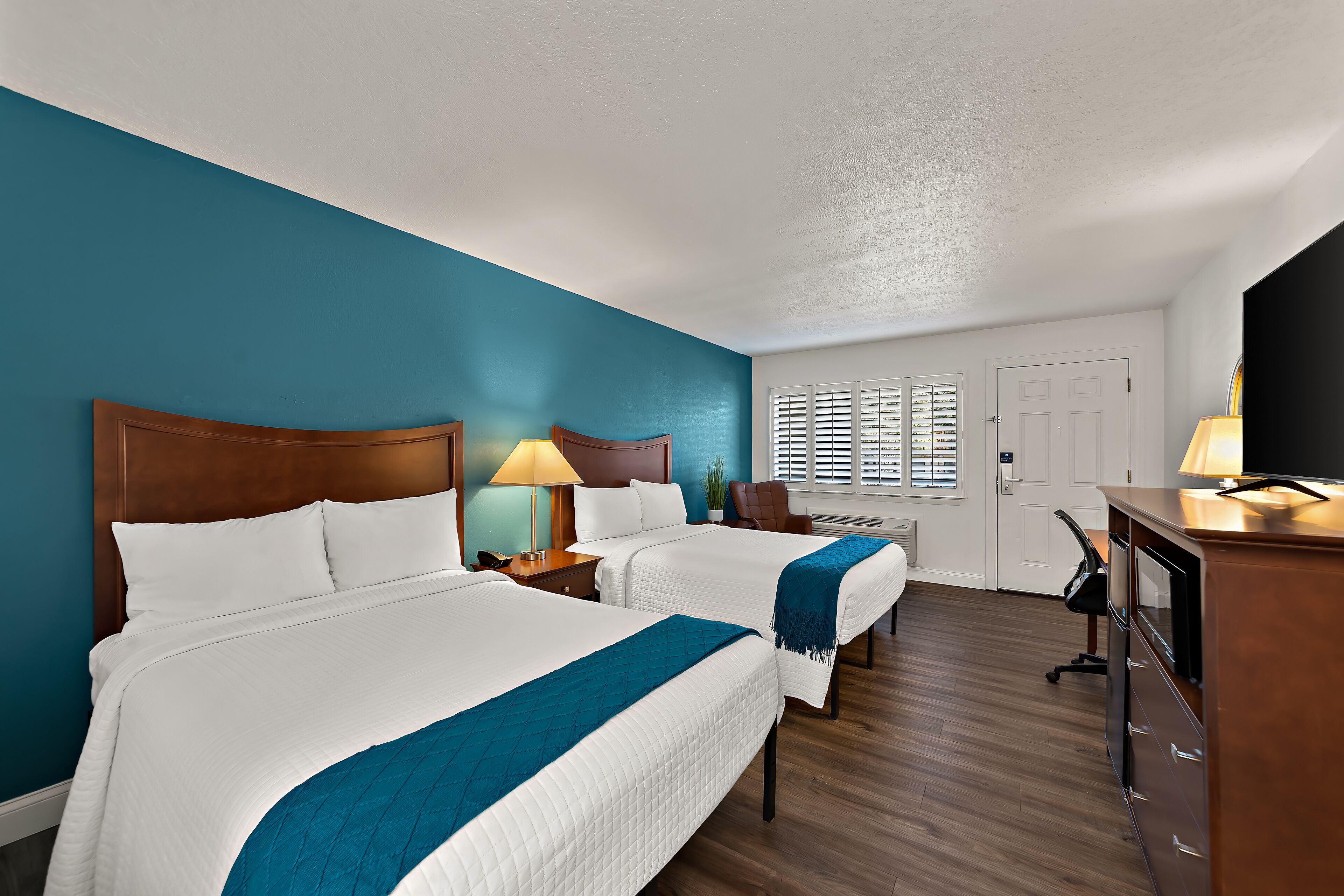 A hotel room with two beds, a desk, and a chair.