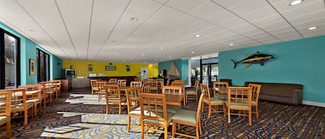A spacious room with a patterned carpet, wooden chairs, and tables arranged for dining.