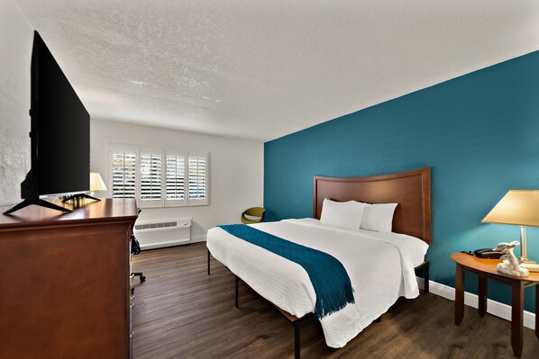 A hotel room with a bed, a desk, a lamp, and a window with blinds. - PaddleTail Waterfront Lodge, Trademark Collection by Wyndham (Crystal River)