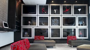 A modern lobby with a grey sofa set, red patterned cushions, and a wall of framed artwork. - Regente Hotel (Mexico City)