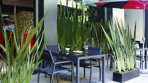 An outdoor seating area with a table and chairs, surrounded by tall green plants. - Regente Hotel (Mexico City)