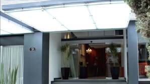 A modern building entrance with a glass canopy, a number '9' sign, and two large potted plants. - Regente Hotel (Mexico City)