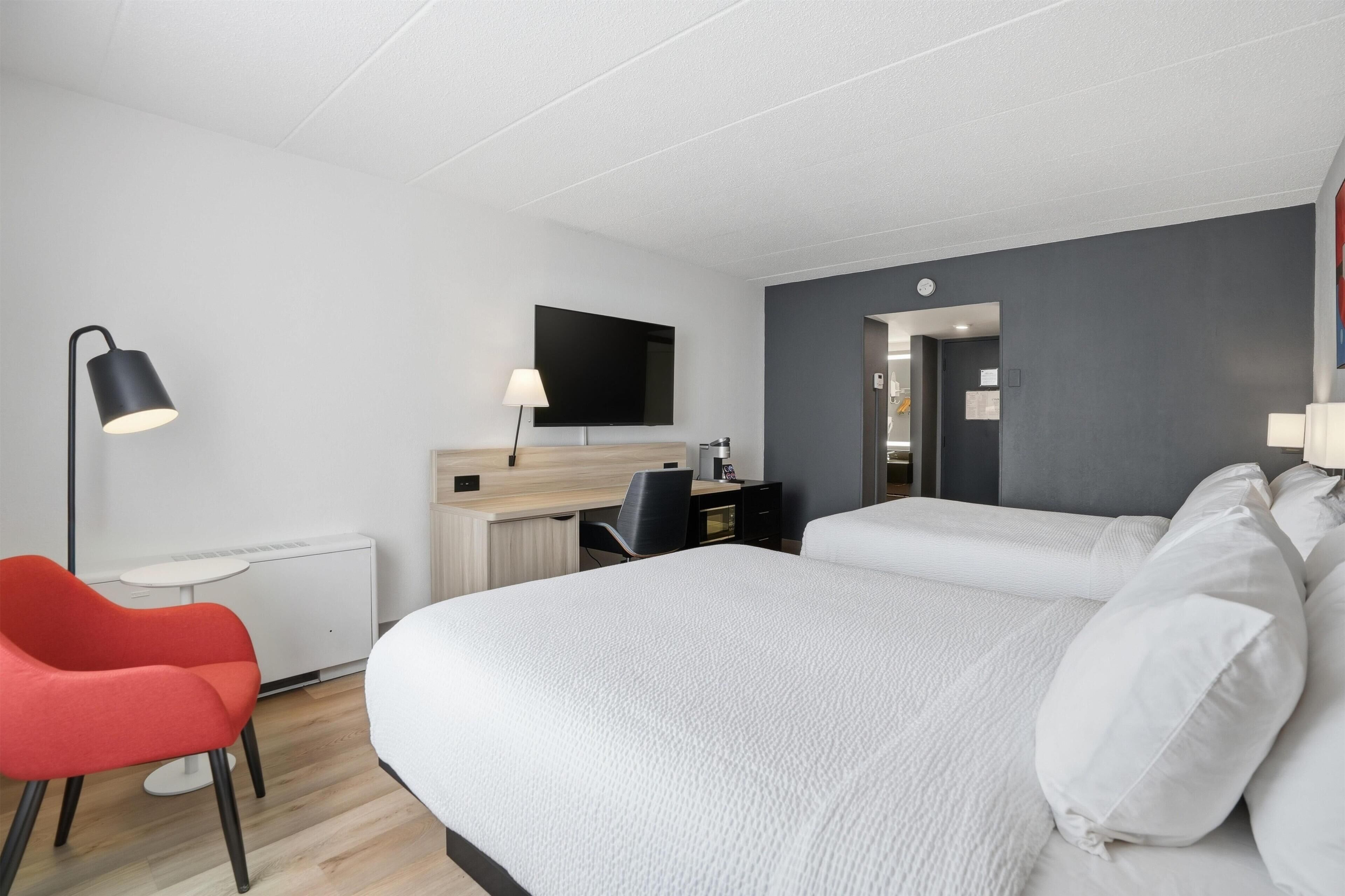 A hotel room with a bed, desk, chair, lamp, and a flat-screen TV.