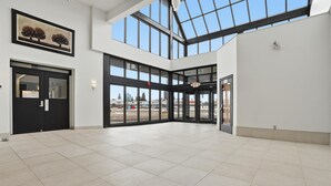 Un vestíbulo amplio con techo alto, ventanas grandes y una puerta que da al exterior.