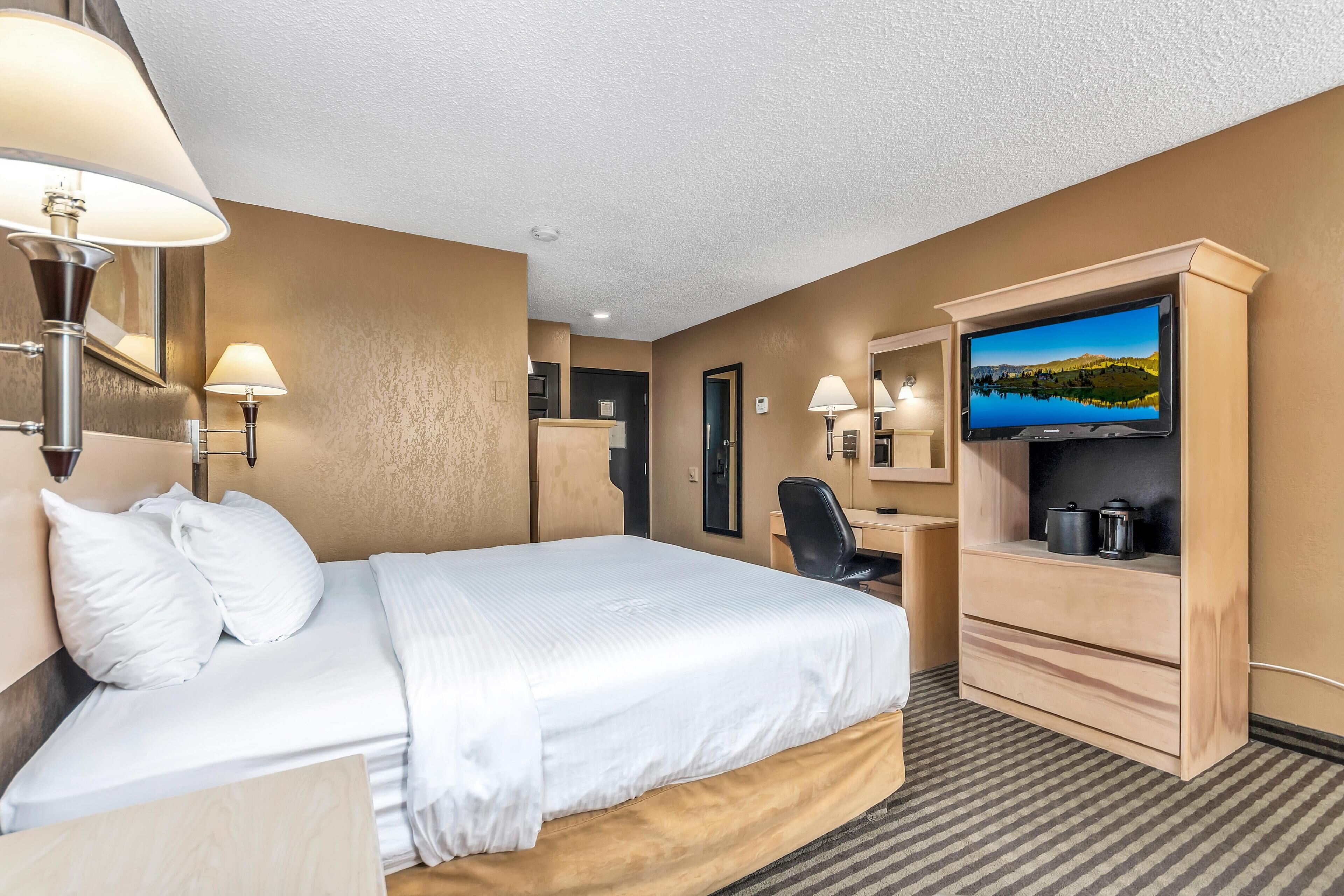 A hotel room with a bed, desk, chair, television, and a view of a lake.