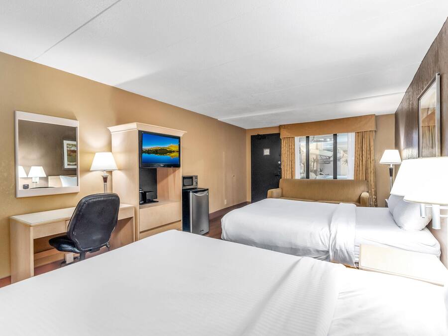 A hotel room with two beds, a desk, a chair, a TV, and a window with curtains.