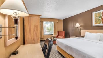 A hotel room with a bed, desk, chair, lamp, and a window with curtains.