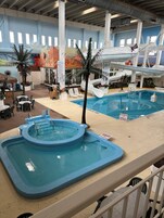 Un área de piscina interior con jacuzzi, sillones de descanso y un tobogán.