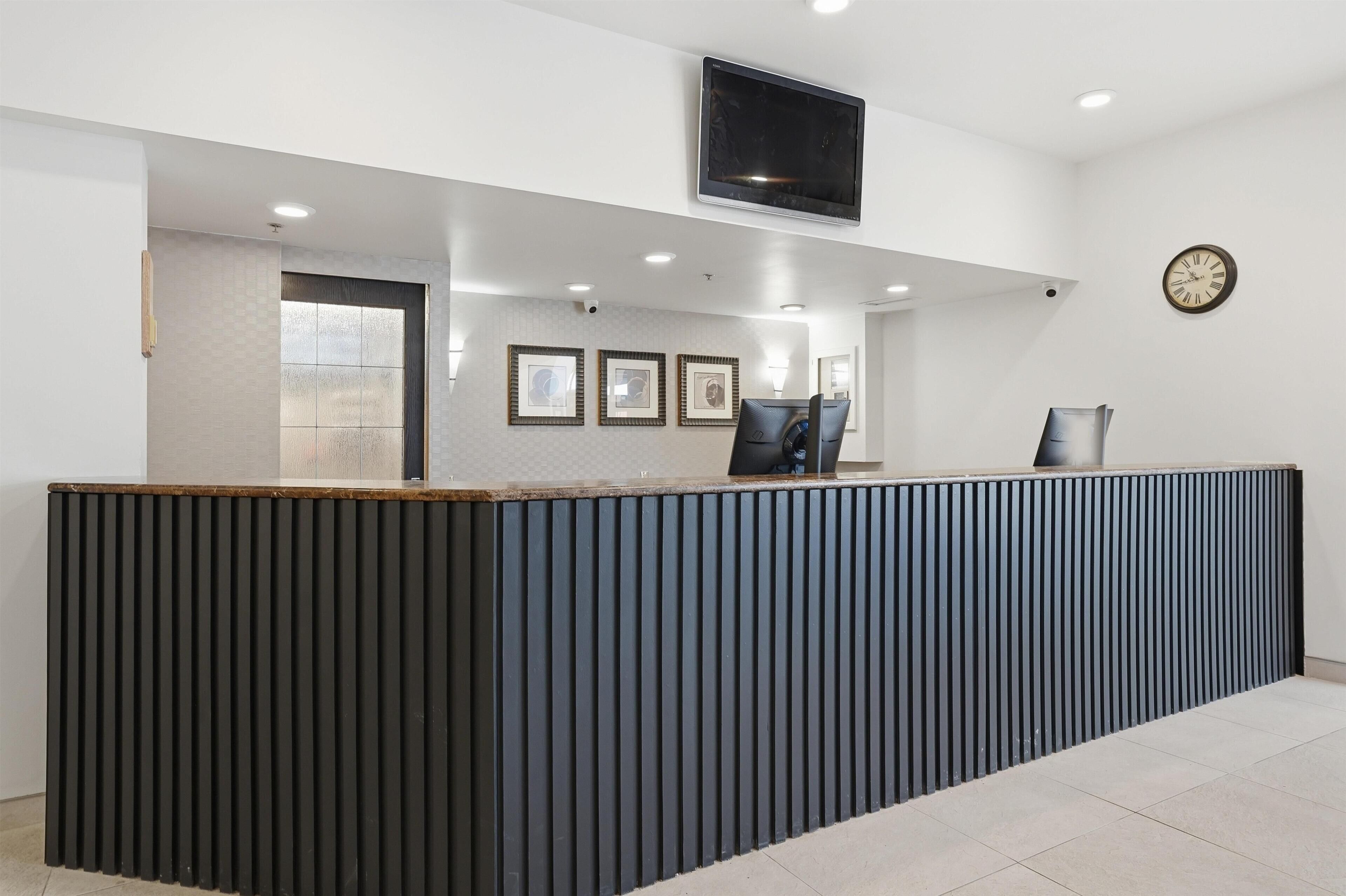 A reception desk with a flat-screen TV, framed pictures, and a clock on the wall.