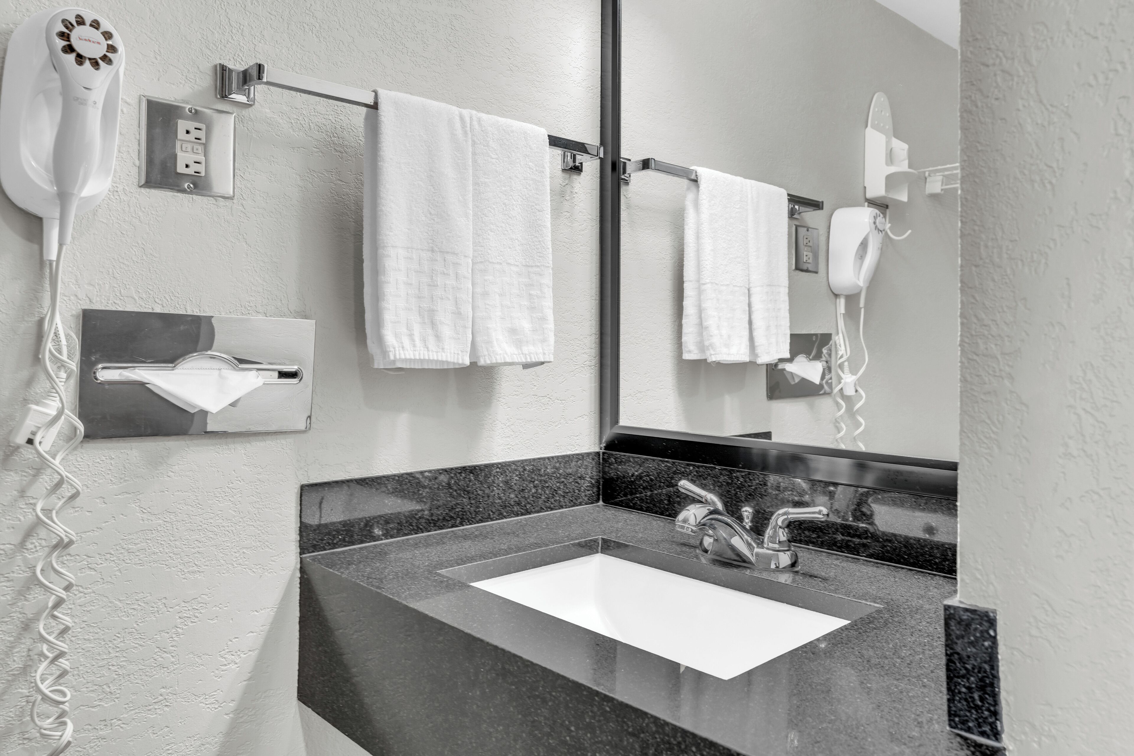 A bathroom with a sink, two towels hanging on a rack, and a hairdryer mounted on the wall.