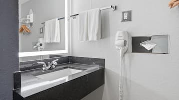 Un baño con lavamanos de superficie negra, un espejo, toalleros con toallas blancas, un secador de pelo y un jabonero.