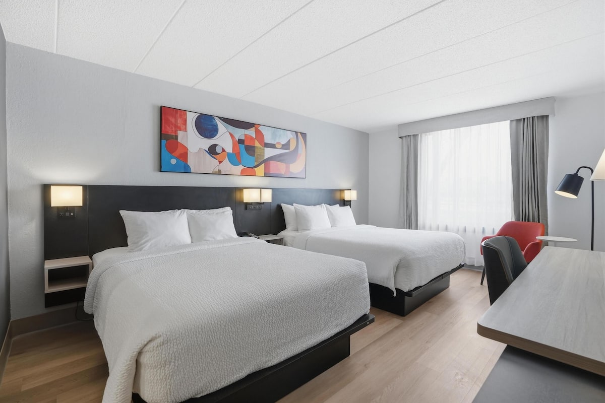 Quarto de hotel com duas camas, uma escrivaninha, uma cadeira e um quadro na parede.