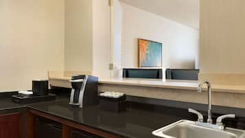 A modern kitchen with a black countertop, stainless steel sink, and a coffee maker.