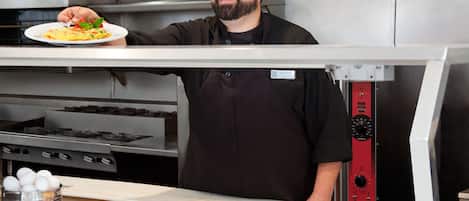 A chef in a kitchen holding a plate of food.