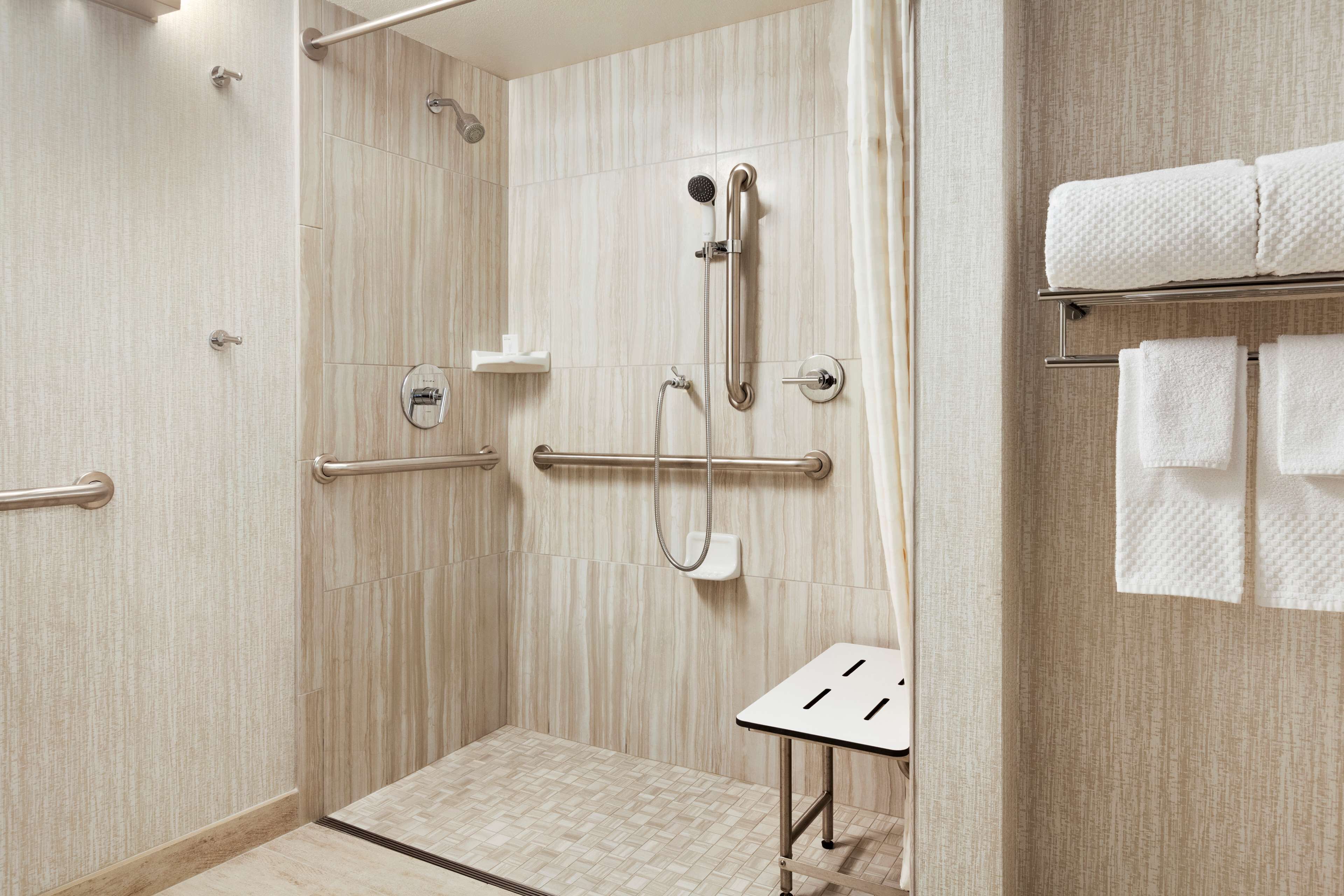 A modern bathroom with a walk-in shower, grab bars, and a towel rack.