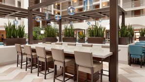 A spacious indoor dining area with a long table, multiple chairs, hanging pendant lights, and potted plants. - Embassy Suites by Hilton San Luis Obispo (San Luis Obispo)
