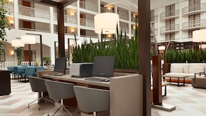 A modern hotel lobby with a central reception desk, multiple seating areas, and a view of the building's interior balconies. - Embassy Suites by Hilton San Luis Obispo (San Luis Obispo)
