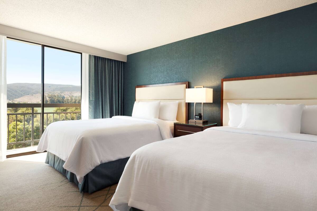 Habitació d'hotel amb dos llits, una finestra gran que ofereix vistes a les muntanyes i una paret d'accent blau fosc.