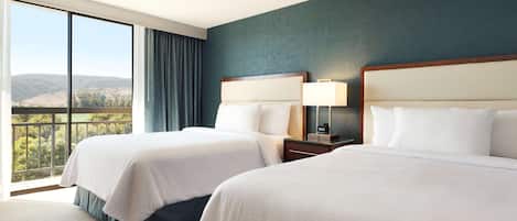 A hotel room with two beds, a large window with a view of the hills, and a dark blue accent wall.