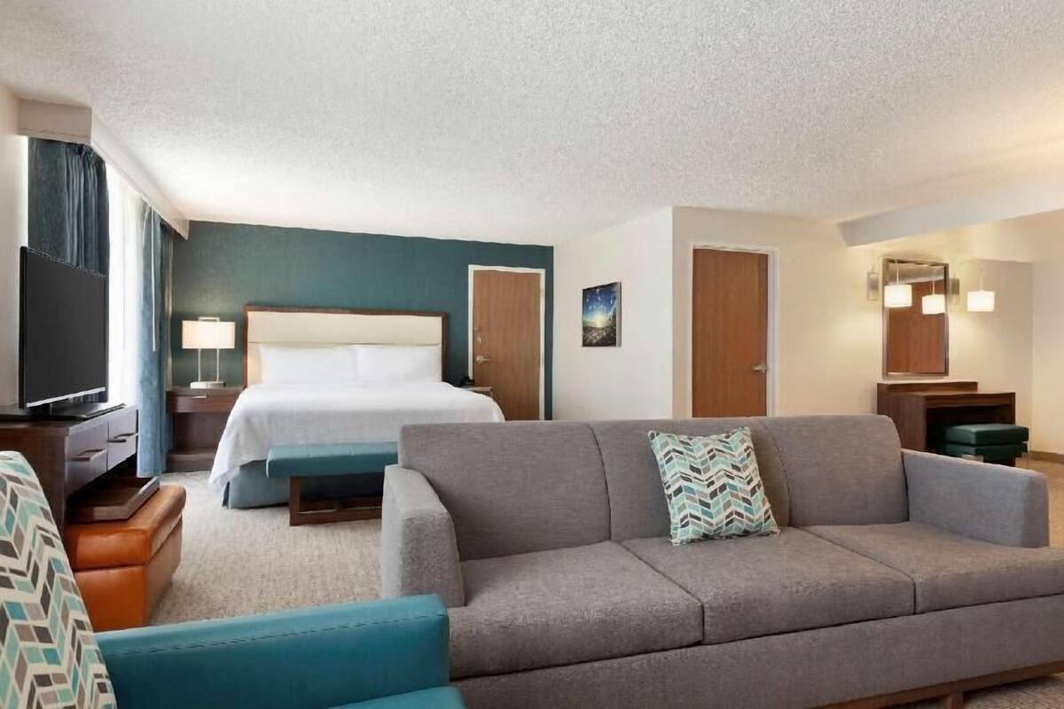 A hotel room with a bed, a sofa, a television, a desk, and a mirror.