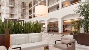 A spacious lobby with a high ceiling, a central seating area with sofas and armchairs, and a large hanging light fixture. - Embassy Suites by Hilton San Luis Obispo (San Luis Obispo)