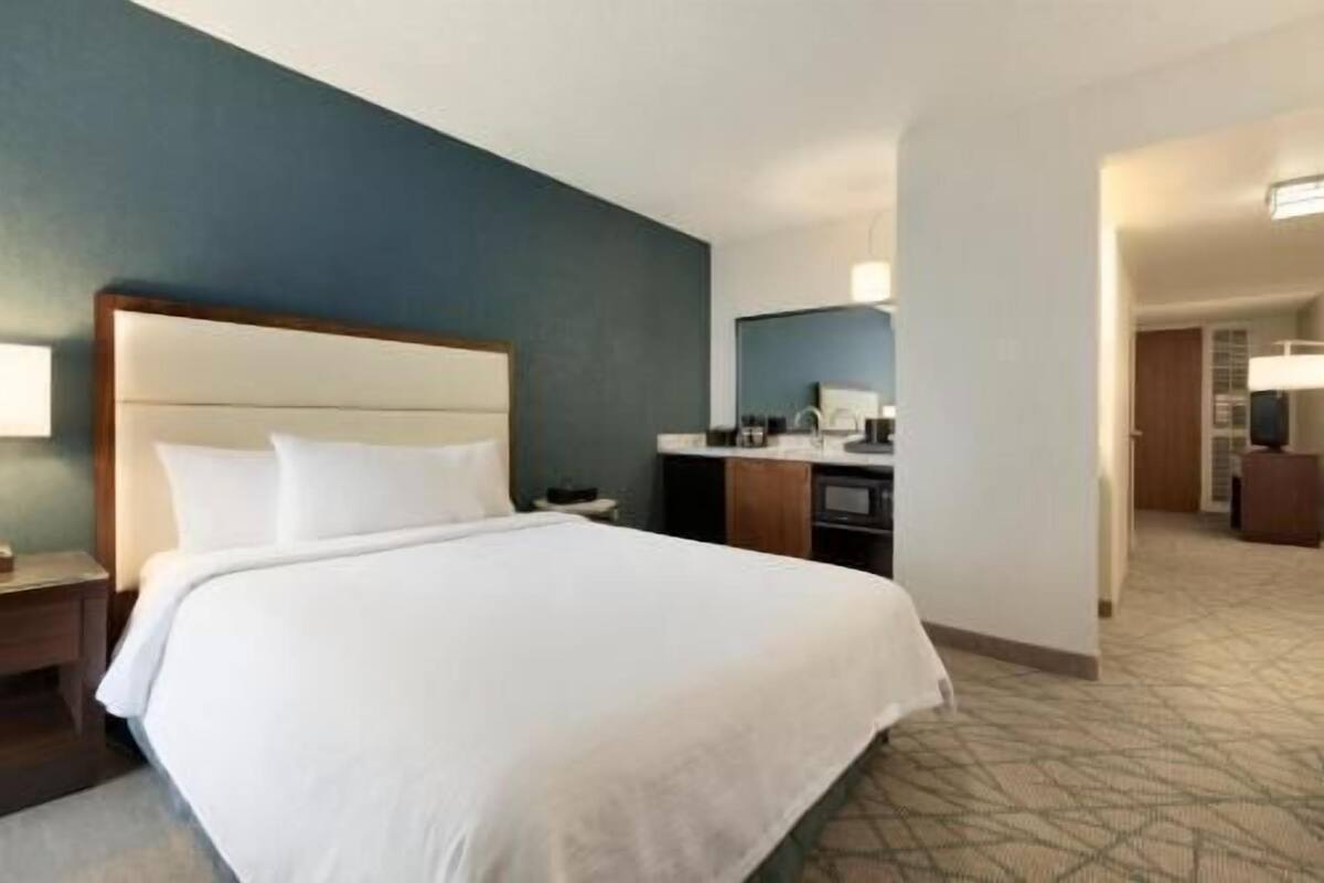A hotel room with a bed, a nightstand, a desk, a mirror, and a television.