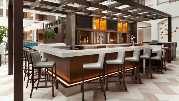 A modern bar area with a long counter, multiple bar stools, and a high ceiling with exposed beams. - Embassy Suites by Hilton San Luis Obispo (San Luis Obispo)