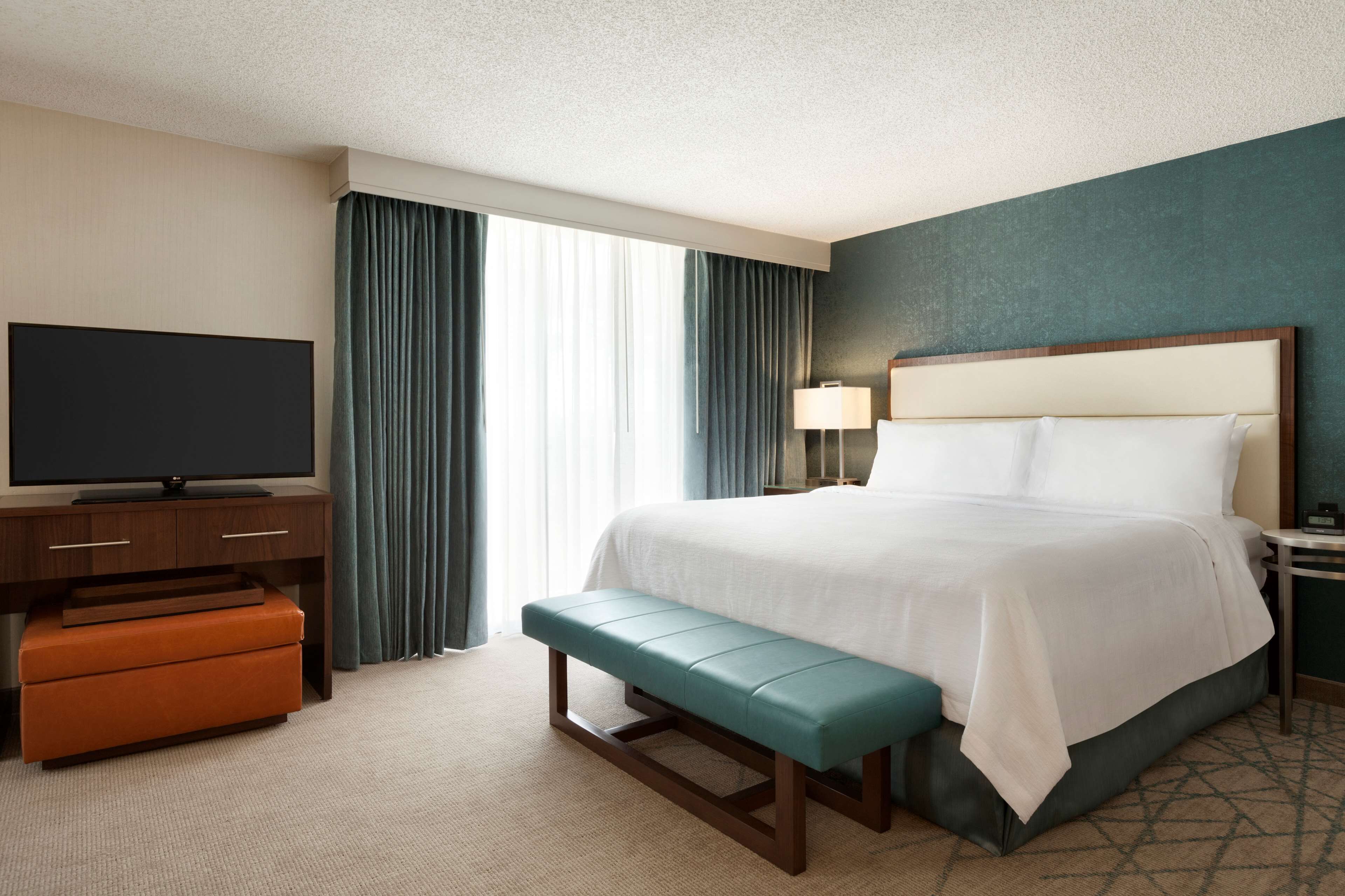 A hotel room with a bed, a television, a bench, and a desk.