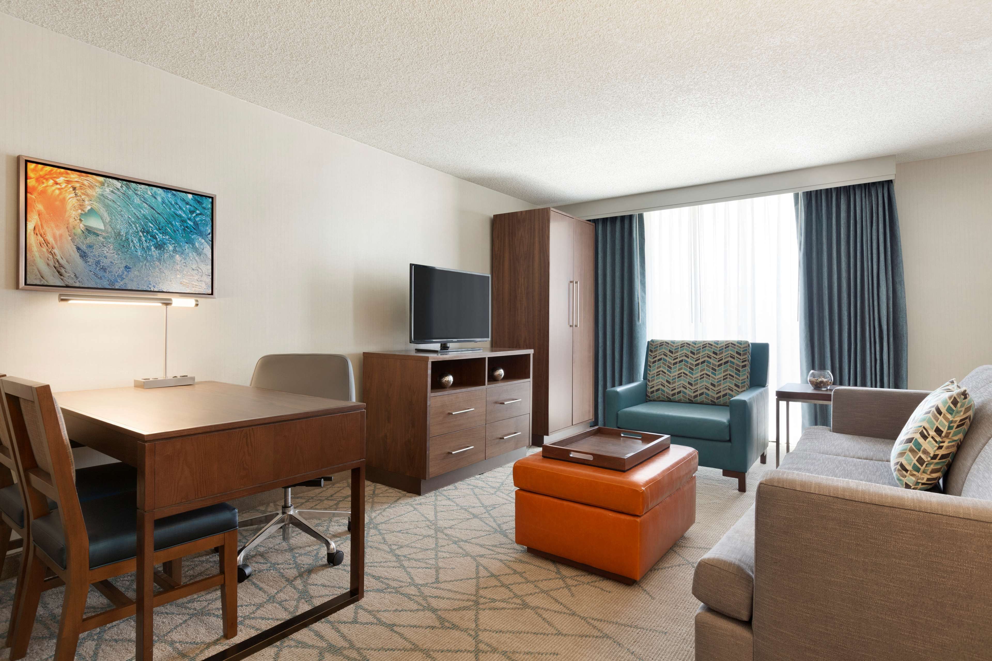 Ein Hotelzimmer mit einem Holztisch, einem Fernseher, einem Sofa und einem fenster mit Vorhängen.
