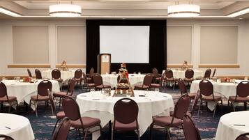 A conference room with round tables, chairs, a projector screen, and a podium.