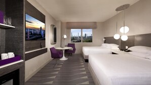 Habitación de hotel con dos camas, televisión, escritorio con silla y vistas a la ciudad.
