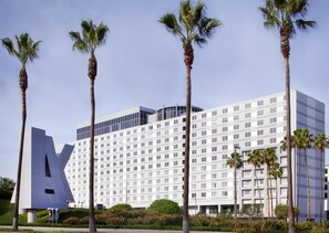 A modern hotel with a large 'A' logo, multiple floors, and palm trees in the foreground.