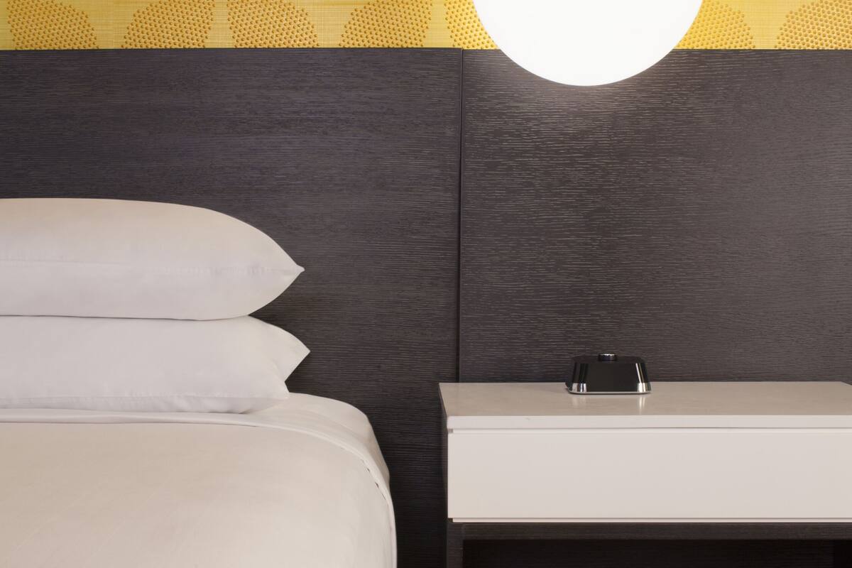Habitación de hotel con una cama, una mesita de noche con lavamanos blanco y una lámpara colgante.