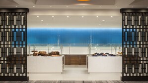Una cocina moderna con vista al océano, que presenta una isla central con diversos alimentos y dos lámparas colgantes encima.
