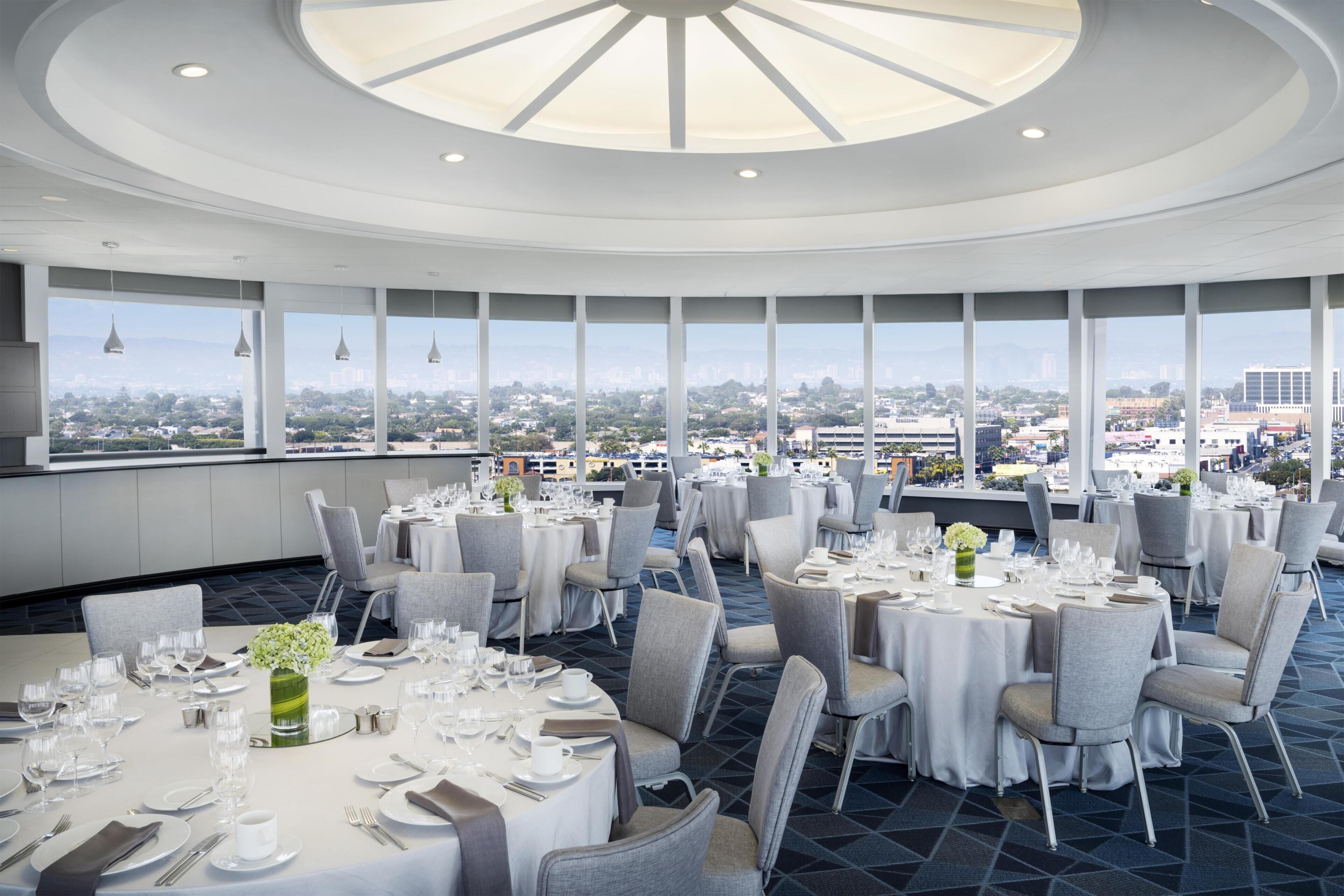 A restaurant with round tables, chairs, and a city view.