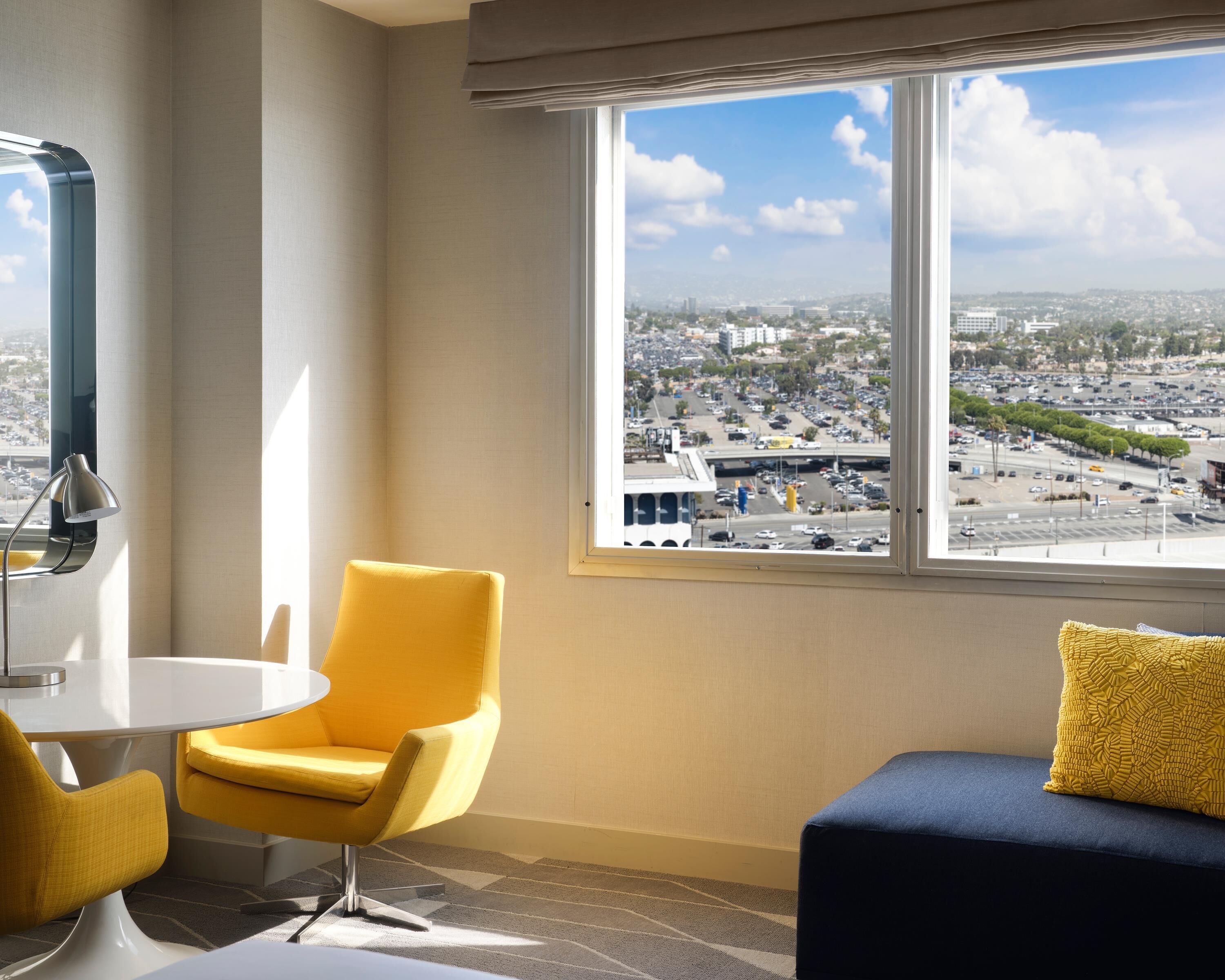 A room with a large window, a yellow chair, a blue sofa, and a white table.