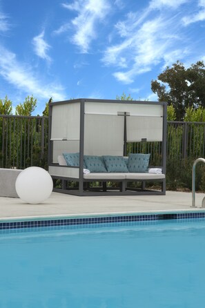 A poolside seating area with a canopy, a large white ball, and a metal pool ladder.