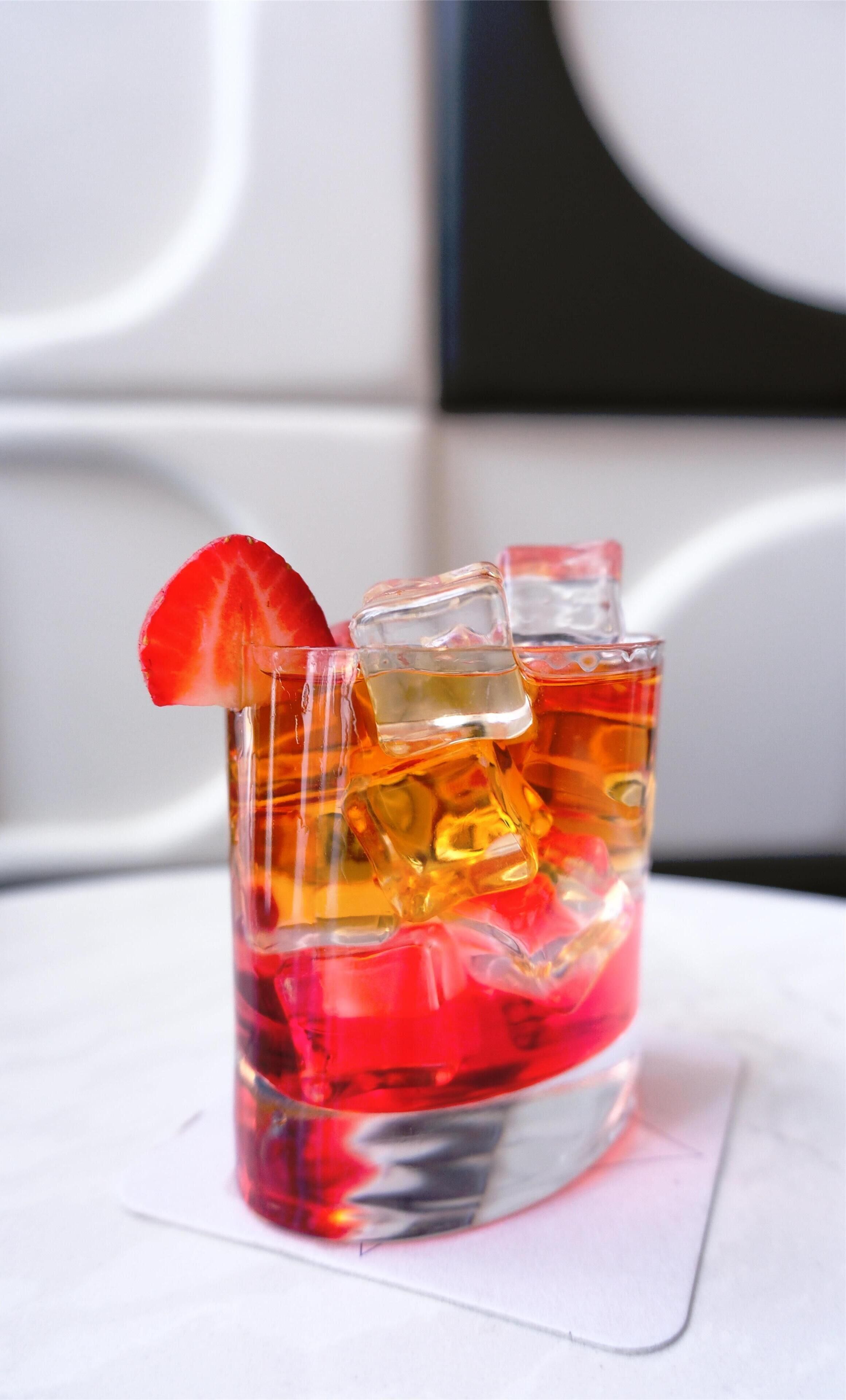 A glass with a red drink, ice cubes, and a strawberry garnish.